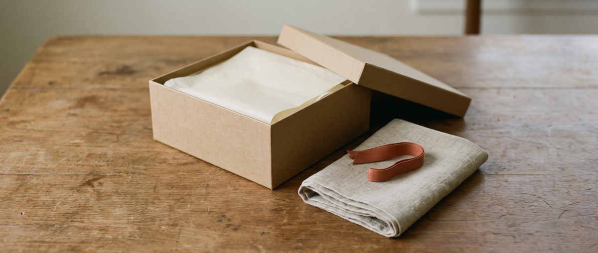 Open kraft box lined with cream tissue paper on a linen surface
